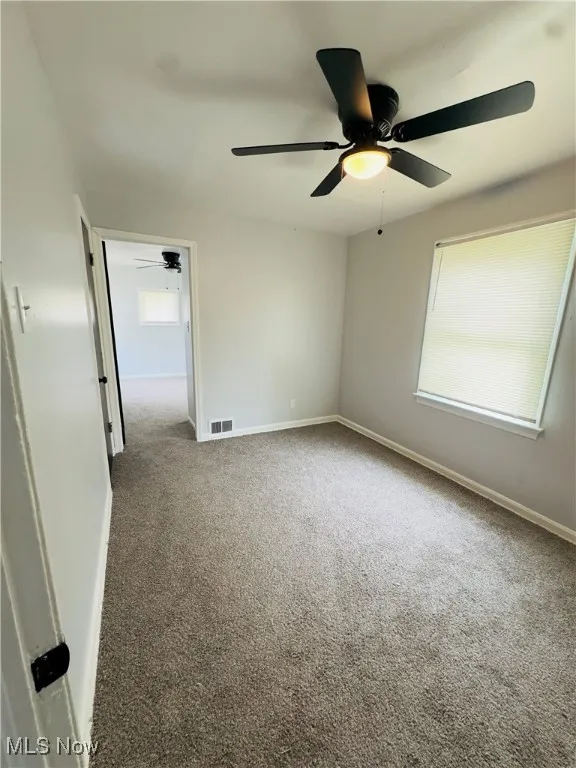 Empty room featuring carpet flooring and a ceiling fan