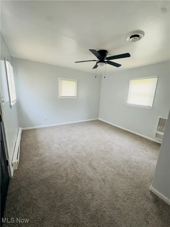 Carpeted spare room with a baseboard heating unit and ceiling fan