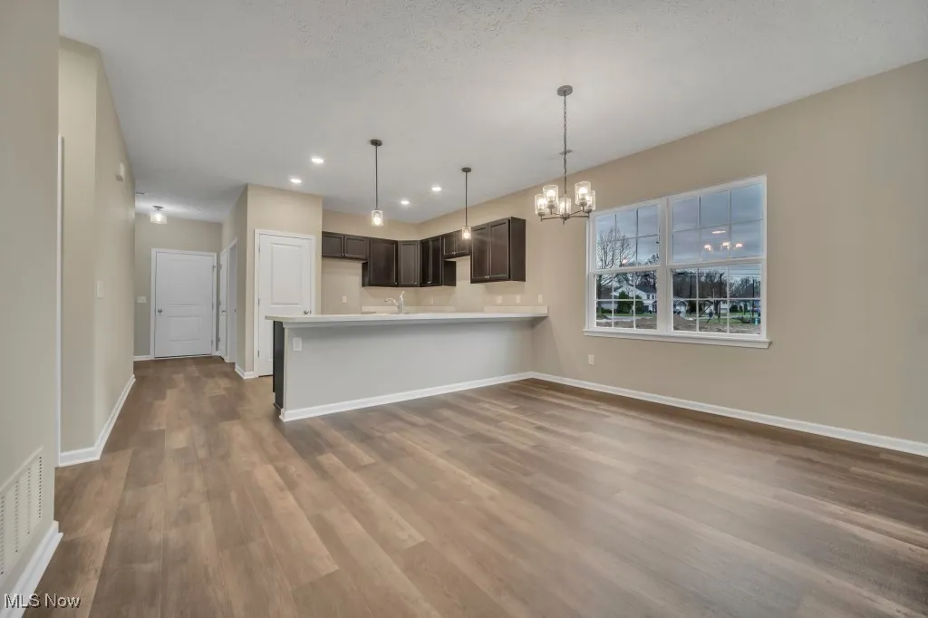 Kitchen with dark wood-style flooring, a peninsula, a chandelier, dark brown cabinets, and light countertops