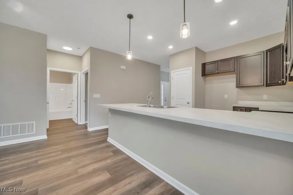 Kitchen with light countertops, dark brown cabinets, hanging light fixtures, dark wood-style flooring, and recessed lighting