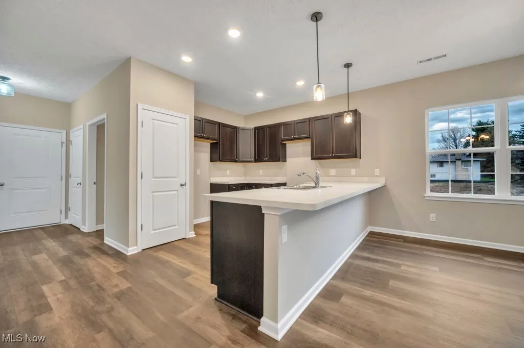 Kitchen with a peninsula, dark wood-type flooring, dark brown cabinetry, recessed lighting, and light countertops