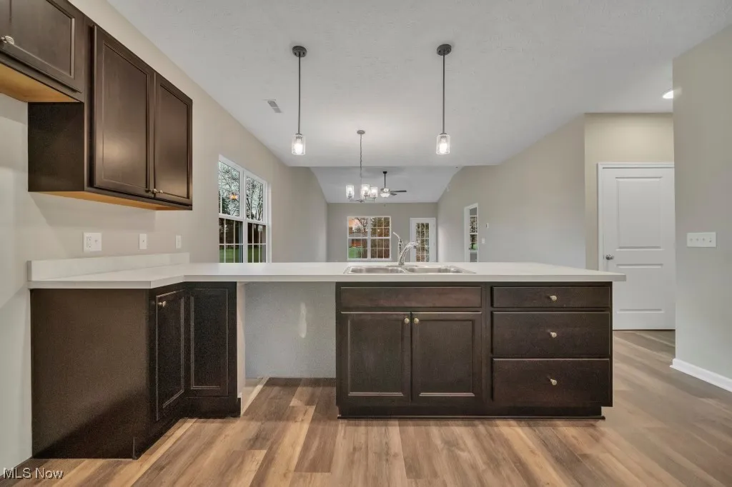 Kitchen with light wood-style flooring, dark brown cabinetry, light countertops, a chandelier, and a peninsula