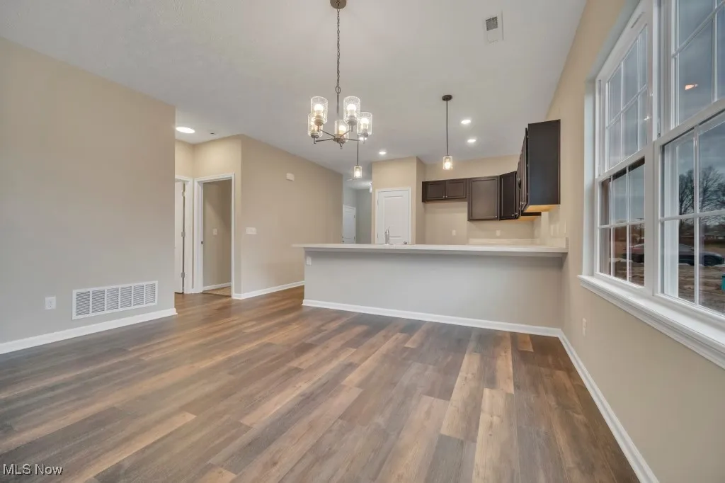 Kitchen featuring a chandelier, dark wood finished floors, a peninsula, light countertops, and pendant lighting
