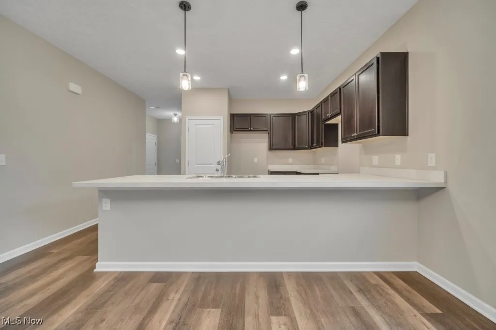 Kitchen featuring dark brown cabinets, wood finished floors, light countertops, a peninsula, and recessed lighting