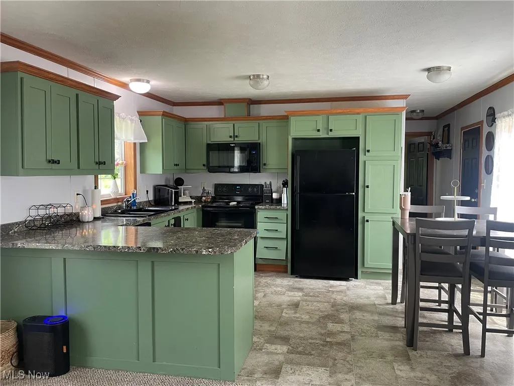 Kitchen featuring black appliances, green cabinetry, crown molding, a peninsula, and stone finish floors