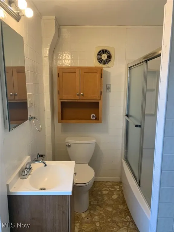 Full bathroom featuring vanity, tile walls, and bath / shower combo with glass door