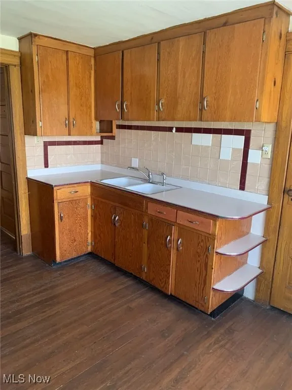 Kitchen with brown cabinets, dark wood-type flooring, backsplash, open shelves, and light countertops