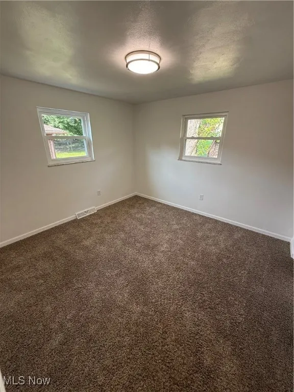Empty room with healthy amount of natural light, dark carpet, and a textured ceiling