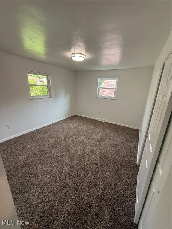 Unfurnished bedroom with multiple windows and dark carpet