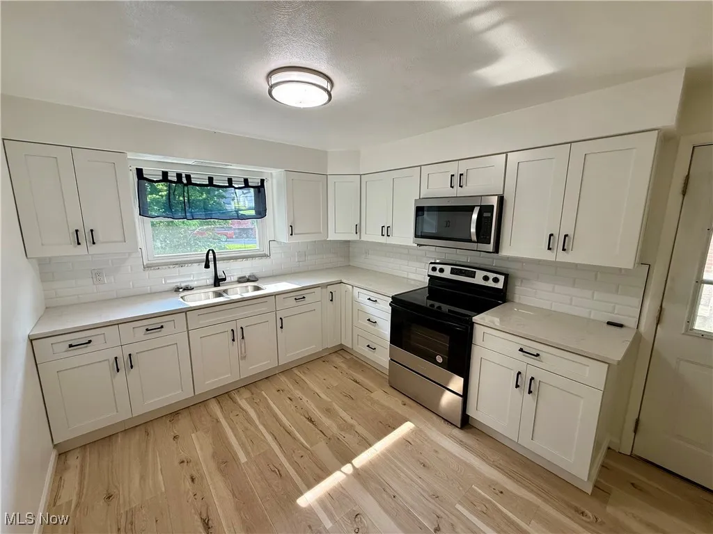 Kitchen with appliances with stainless steel finishes, light wood-type flooring, and white cabinetry