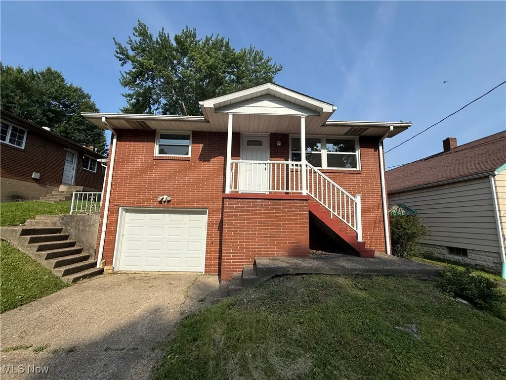 View of front facade with stairway, concrete driveway, brick siding, and a garage