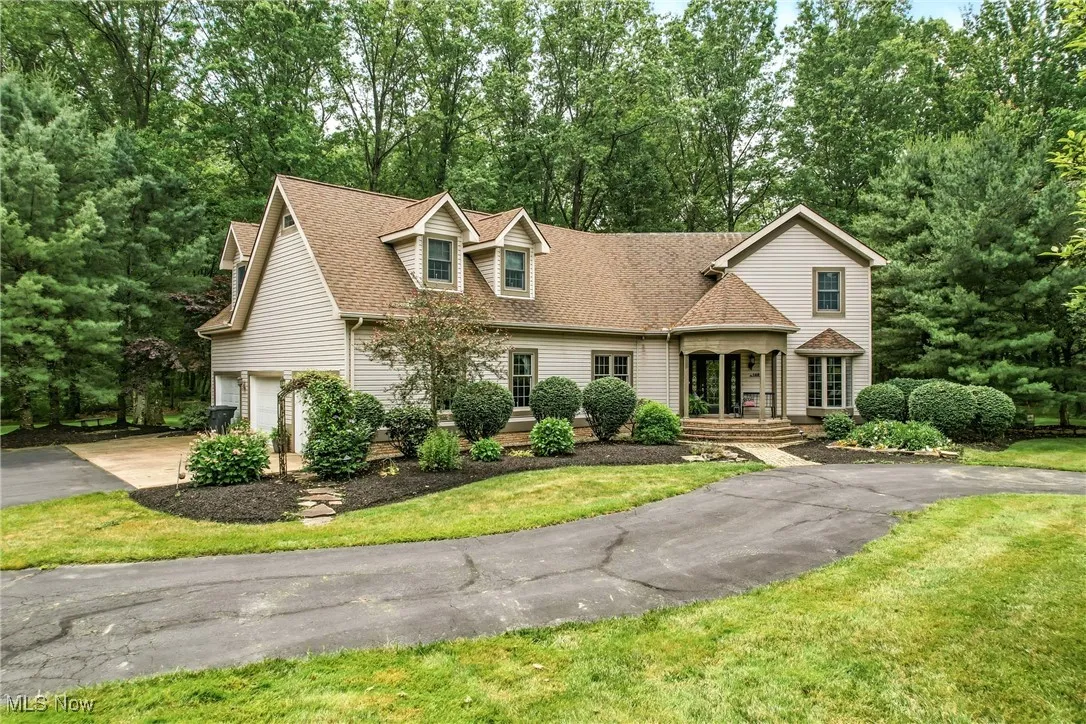 View of front of home featuring a garage, driveway, a shingled roof, a front yard, and view of scattered trees