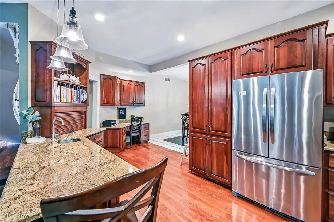 Kitchen featuring freestanding refrigerator, recessed lighting and wood floors, light stone countertops, and pendant lighting