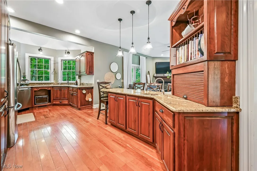 Kitchen with wood flooring, pendant lighting, appliances with stainless steel finishes, light stone counters, and a kitchen bar