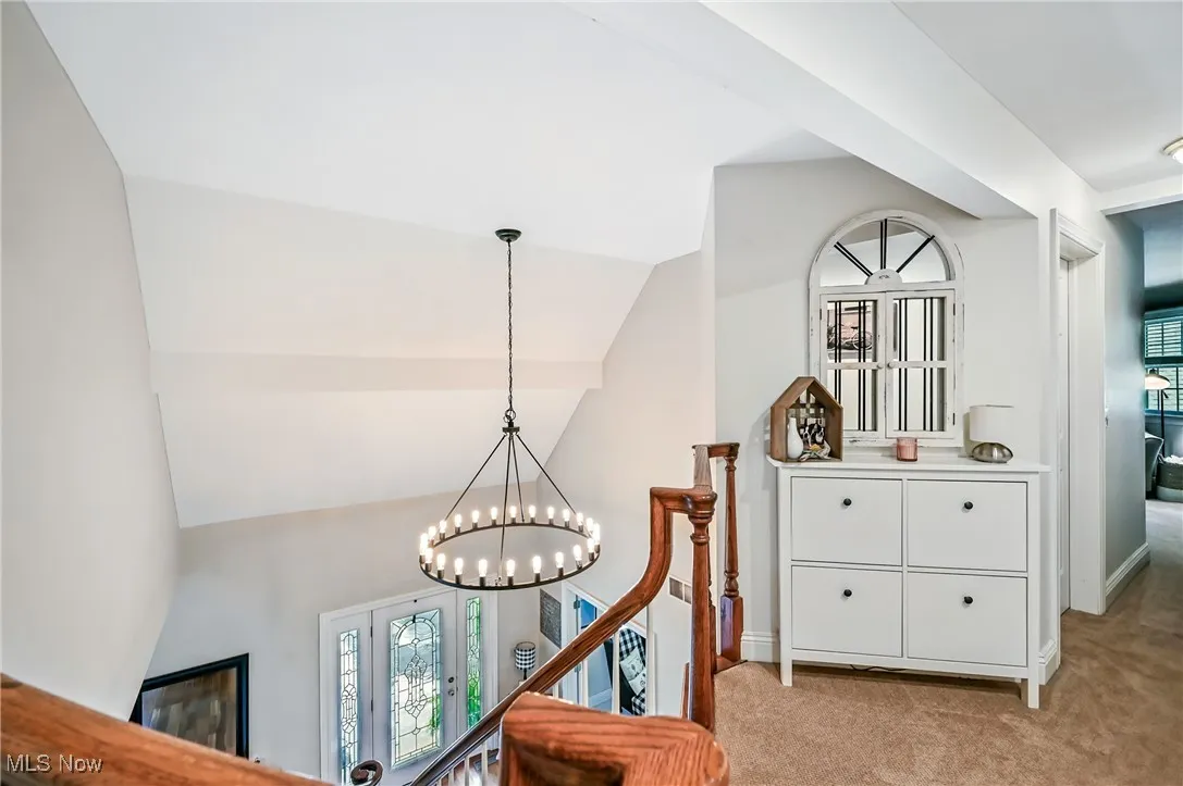 Hall featuring an upstairs landing, light colored carpet, healthy amount of natural light, and a chandelier