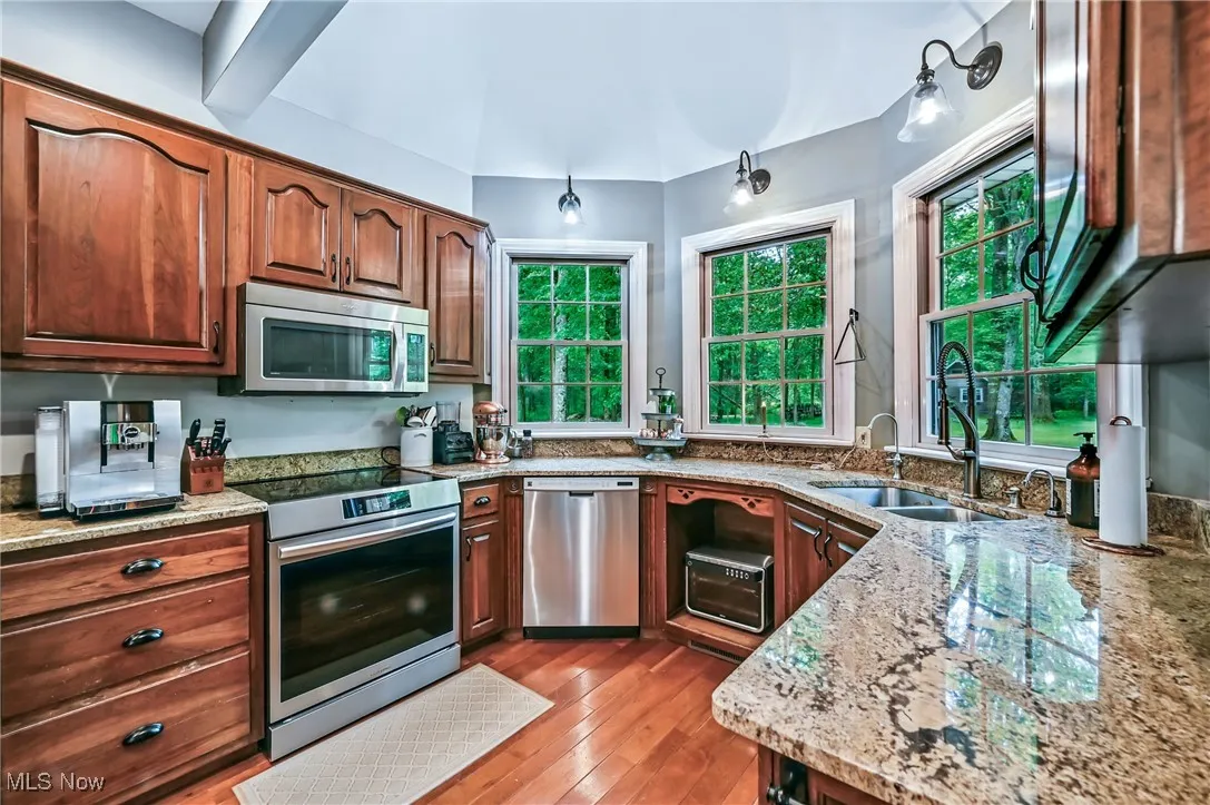 Kitchen with appliances with stainless steel finishes, light stone counters, and wood flooring