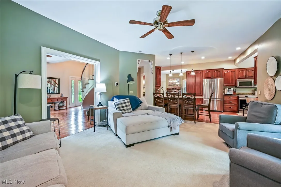 Living area featuring a ceiling fan, stairs, recessed lighting, light colored carpet, and wood flooring