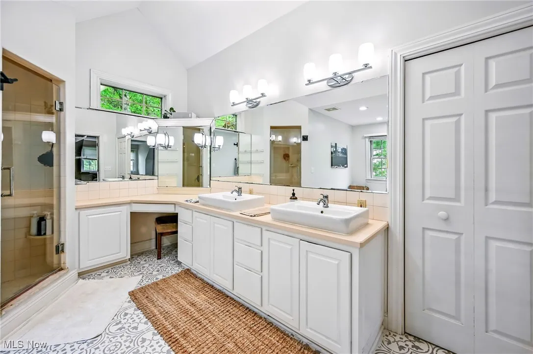 Full bath featuring a stall shower, double vanity, and vaulted ceiling