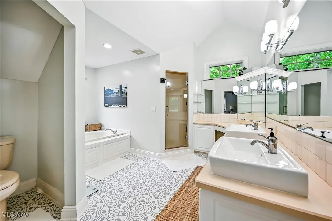Bathroom with a bath, vanity, a stall shower, vaulted ceiling, and tile patterned flooring