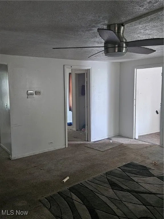 Carpeted empty room featuring ceiling fan and a textured ceiling
