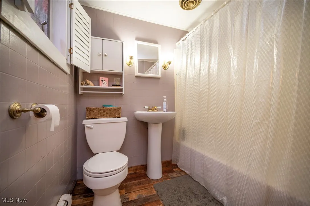 Bathroom with wood finished floors, shower / bathtub combination with curtain, tile walls, and baseboard heating
