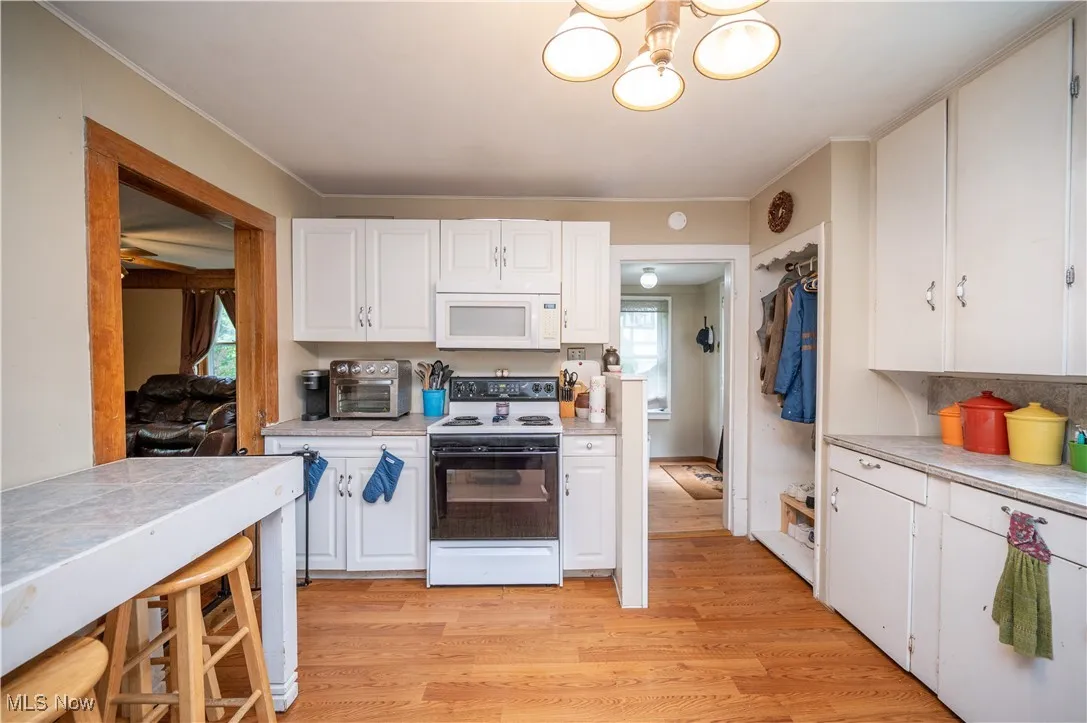 Kitchen with white microwave, electric range oven, light countertops, white cabinets, and crown molding