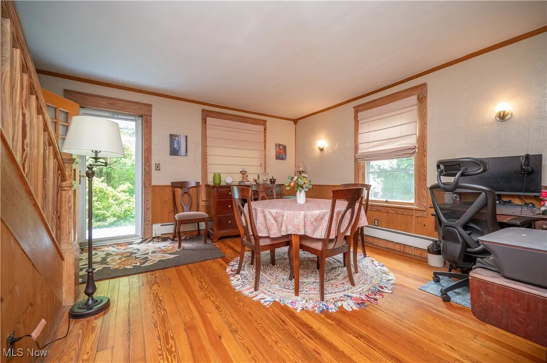 Dining space featuring ornamental molding, light wood-style floors, a wainscoted wall, a baseboard heating unit, and wooden walls