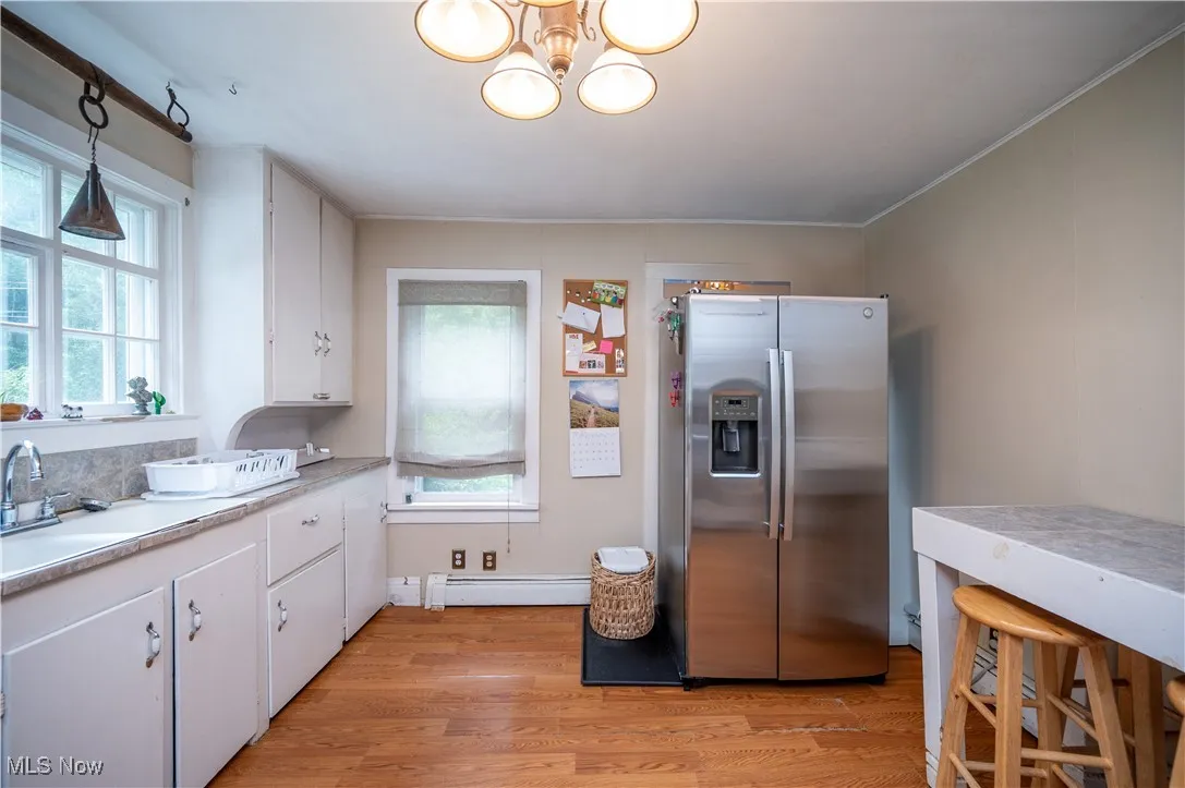 Kitchen with stainless steel fridge, baseboard heating, plenty of natural light, and white cabinetry