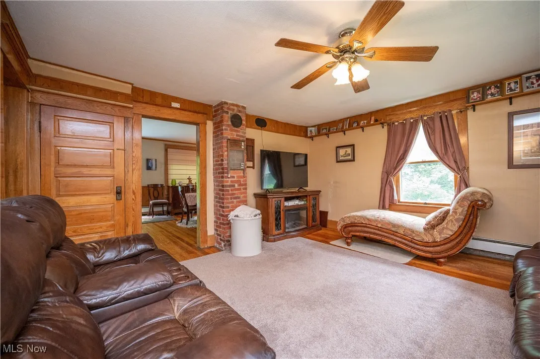 Living area featuring wood finished floors, a ceiling fan, a baseboard heating unit, and a fireplace