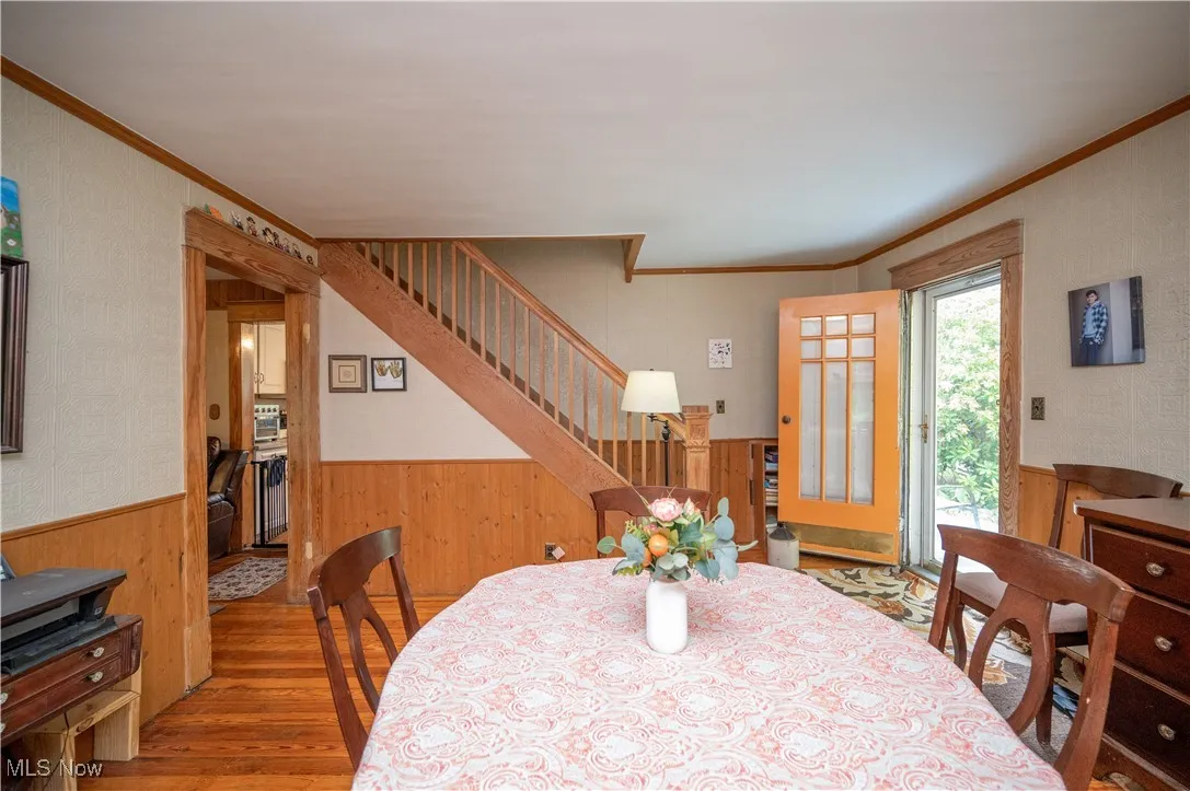 Dining space with a wainscoted wall, wood finished floors, ornamental molding, wood walls, and stairway