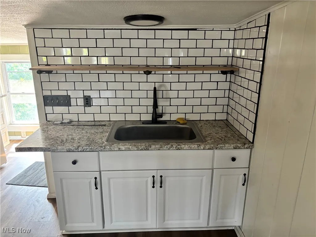 Kitchen with a textured ceiling, white cabinetry, backsplash, and wood finished floors