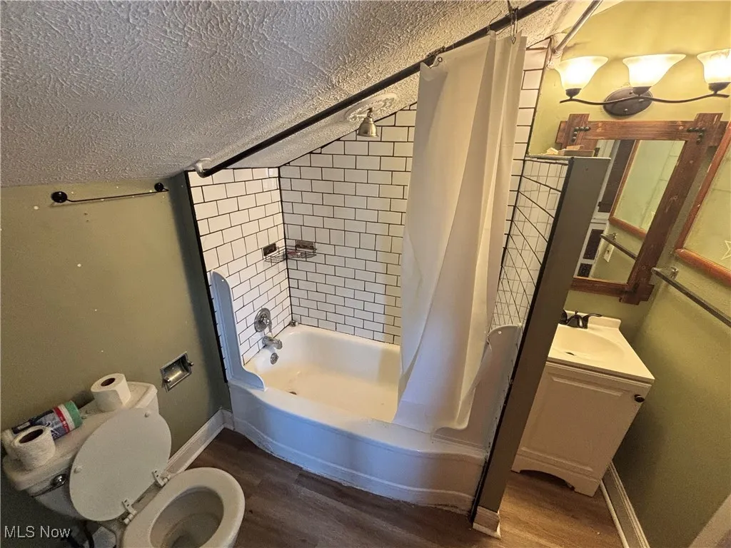 Bathroom with a textured ceiling, wood finished floors, shower / tub combo, and vanity