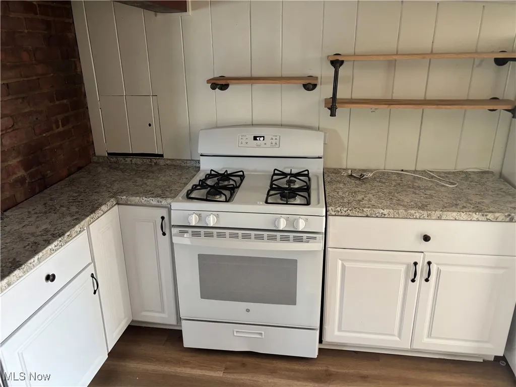 Kitchen with white range with gas cooktop, dark wood-type flooring, white cabinets, and light stone countertops