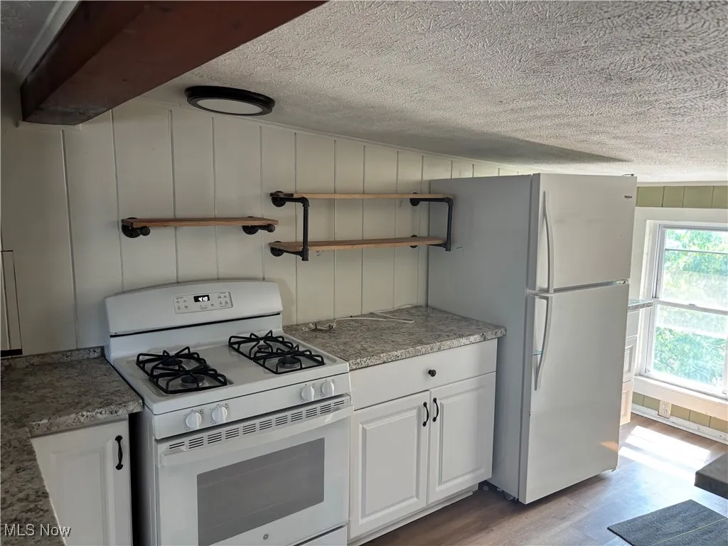 Kitchen featuring white appliances, light wood-style flooring, a textured ceiling, open shelves, and white cabinets