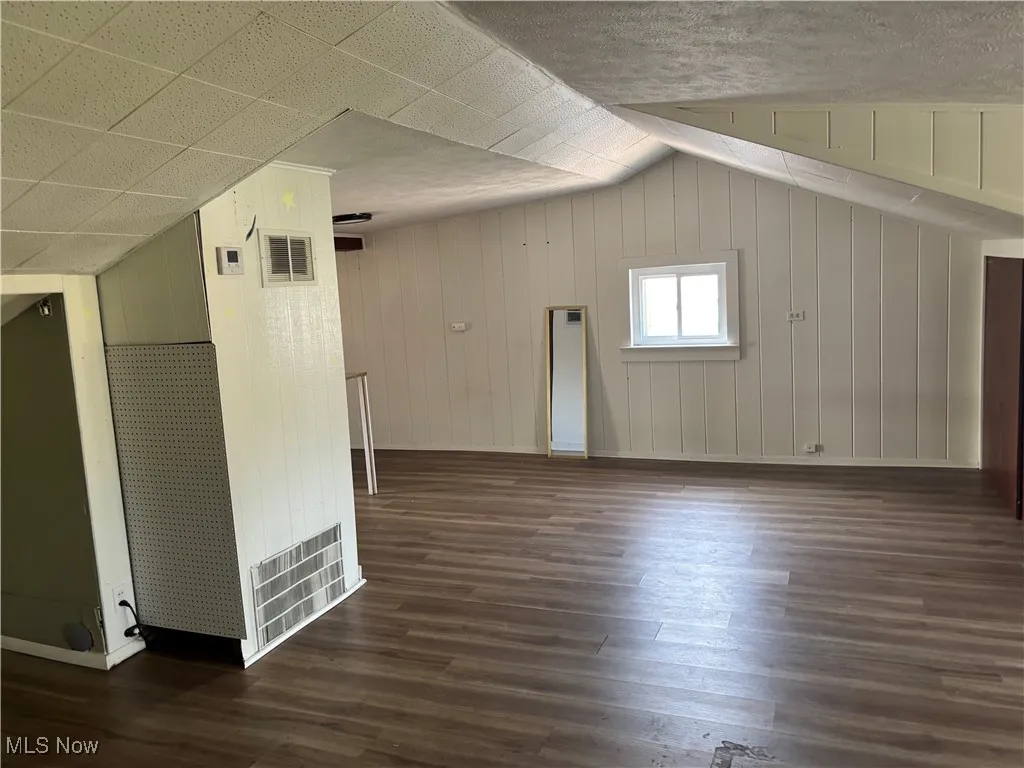 Additional living space with dark wood-style floors, lofted ceiling, and wood walls