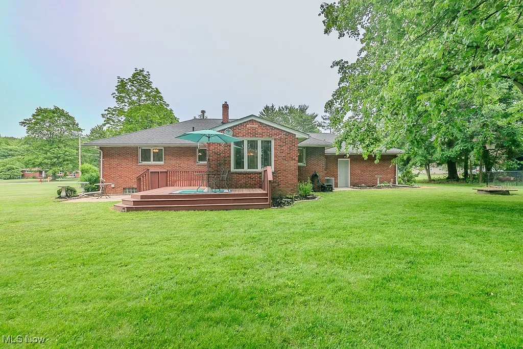 Rear view of property with a wooden deck, a lawn, brick siding, and a chimney