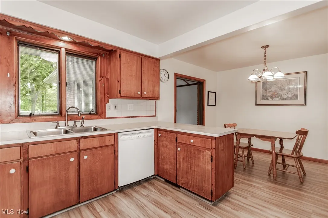 Kitchen featuring dishwasher, a peninsula, light wood-style flooring, light countertops, and a chandelier in dining area