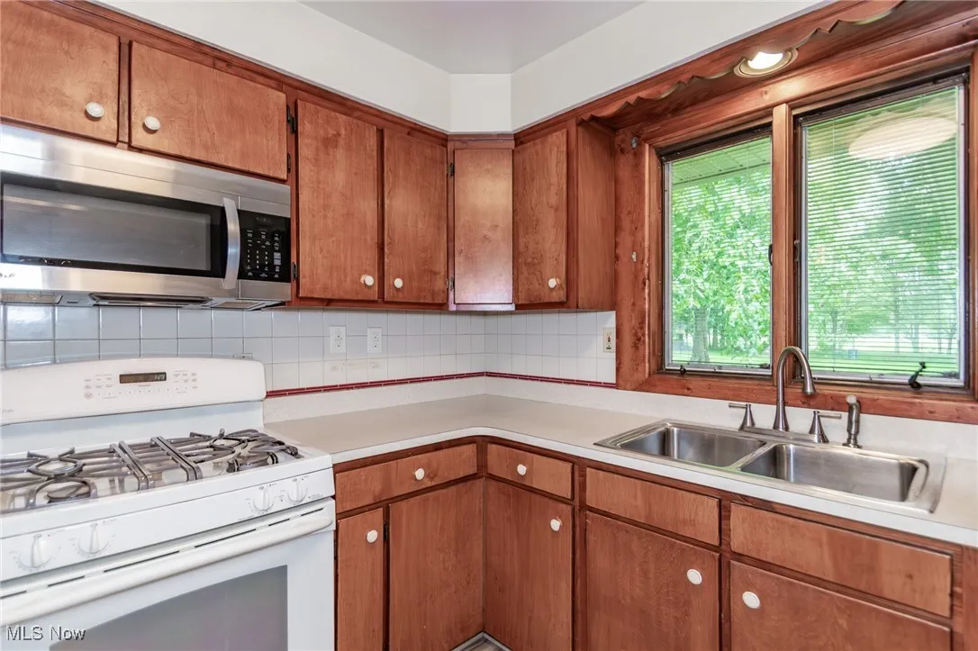 Kitchen with white gas range oven, stainless steel microwave, light countertops, and decorative backsplash
