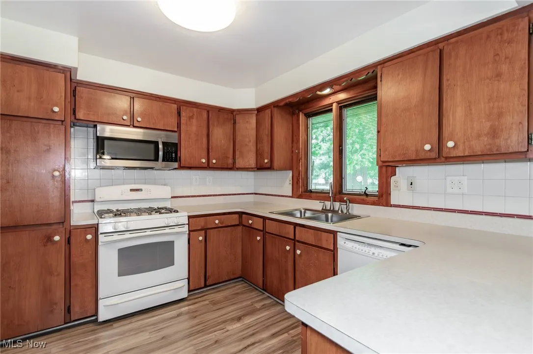 Kitchen featuring white appliances, light countertops, brown cabinetry, and backsplash