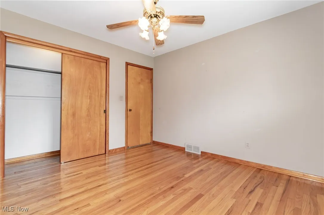 Unfurnished bedroom with light wood-style flooring, multiple closets, and ceiling fan