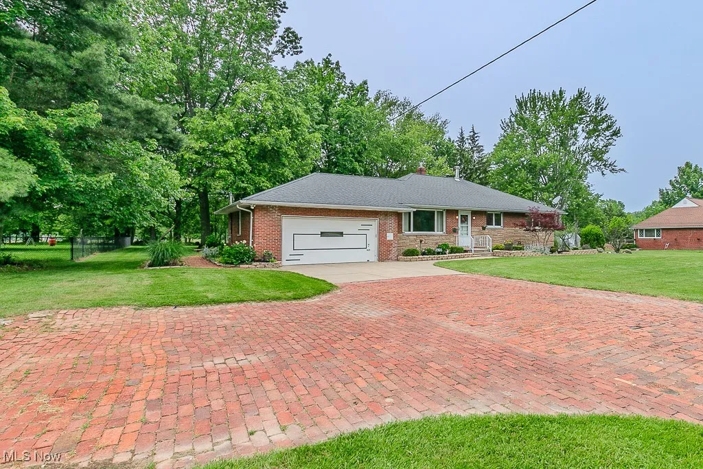 Ranch-style home featuring an attached garage, decorative driveway, brick siding, and a chimney