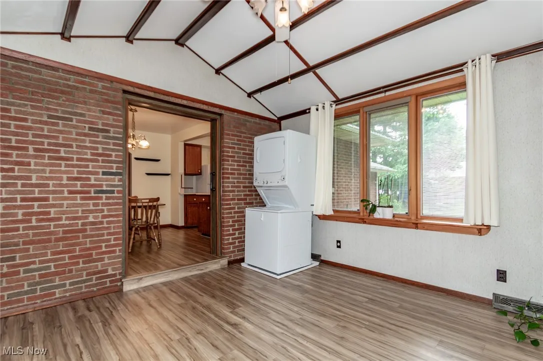Family room featuring vaulted ceiling, light wood-style flooring, stacked washer and clothes dryer, brick wall, and a chandelier