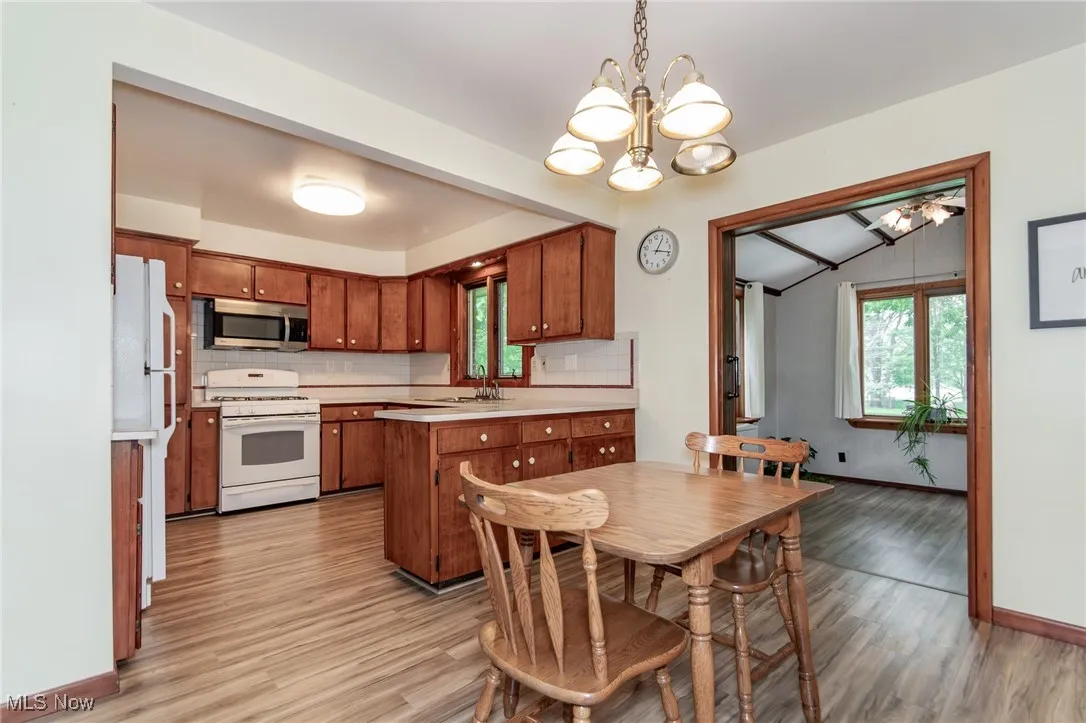 Kitchen and dining area featuring gas range gas stove, stainless steel microwave, a chandelier, brown cabinetry, and light wood finished floors