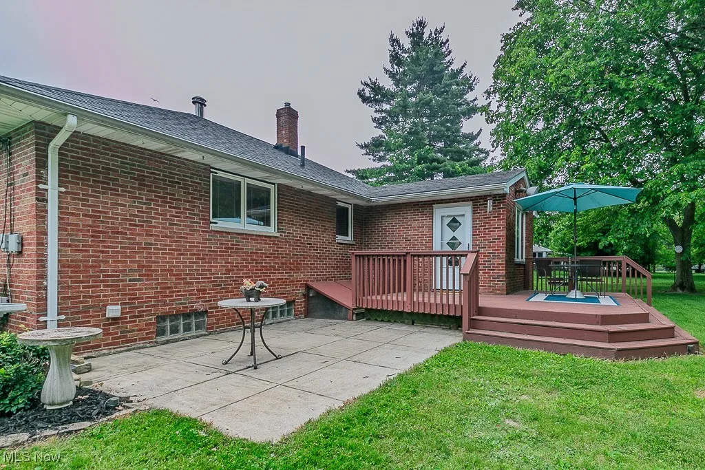 Rear view of house with a patio area, a lawn, a deck, brick siding, and a chimney