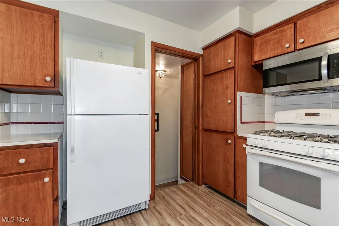 Kitchen with white appliances, light wood-style flooring, light countertops, brown cabinetry, and backsplash