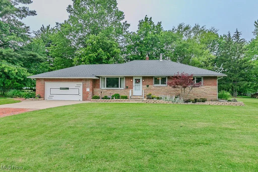 Ranch-style home featuring concrete and brick driveway, an attached garage, a front yard and brick and stone siding