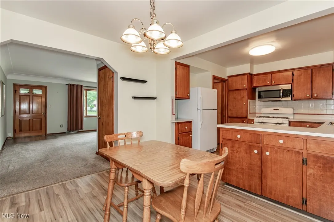 Kitchen with white appliances, a chandelier, light countertops, light wood finished floors, and brown cabinetry