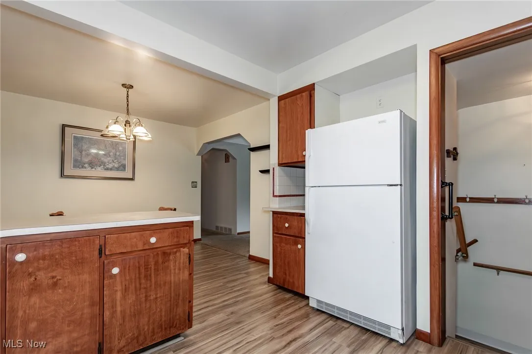 Kitchen featuring refrigerator, light countertops, light wood-type flooring, brown cabinets, and view of stairs to basement.