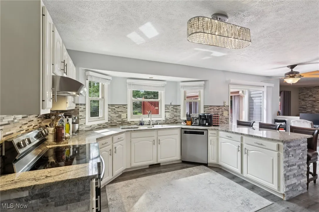 Kitchen with stainless steel appliances, exhaust hood, a peninsula, light wood finished floors, and a textured ceiling