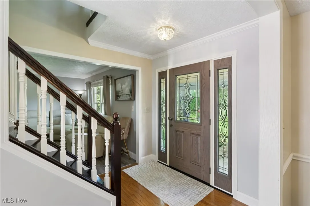 Foyer featuring wood finished floors, stairway, a textured ceiling, and crown molding